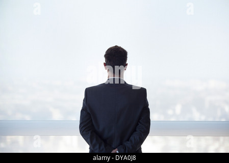 Businessman looking out high rise window at view of city below, rear view Stock Photo