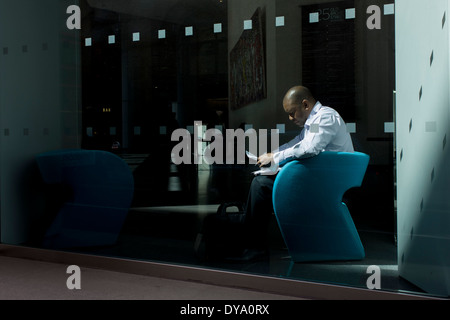 A businessman sits reading documents in sunlight by the wondow of a company foyer in the City of London, the capital's financial district. Stock Photo