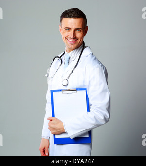 Happy male doctor holding empty clipboard on gray background Stock Photo