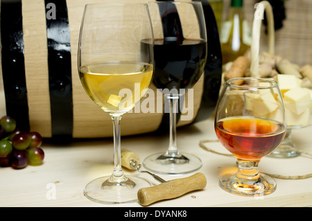 Red and white wine in glasses, brandy. On the background of a barrel and wine corks basket, bowl with cheese and a bottle of win Stock Photo