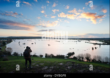 A photographer records the scene as dawn breaks over the flooded fields of the Somerset Levels with water pouring from the River Stock Photo