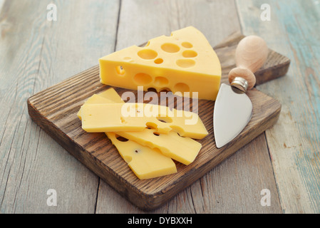 Cheese with big holes and knife on wooden cutting board Stock Photo