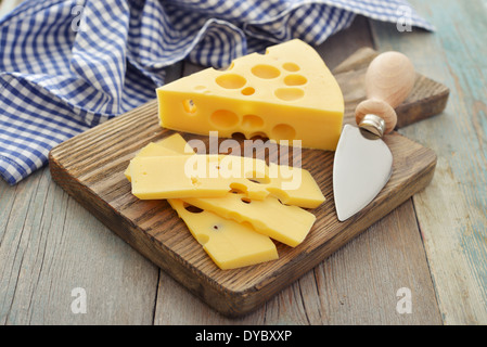 Cheese with big holes and knife on wooden cutting board Stock Photo