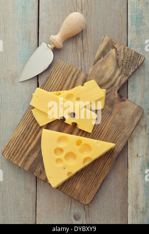 Cheese with big holes and knife on wooden cutting board Stock Photo