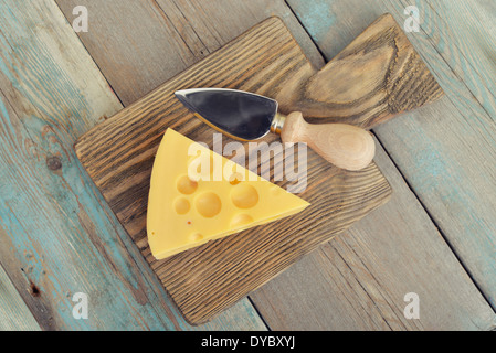 Cheese with big holes and knife on wooden cutting board Stock Photo