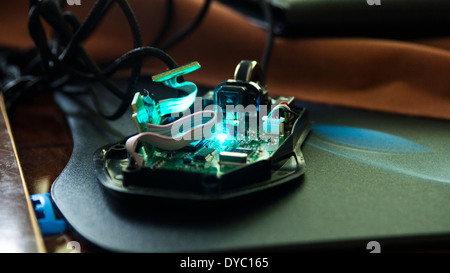 Computer PC mouse dismantled taken apart inside circuit mouse wheel board cables wires mouse mat wooden table led light glowing Stock Photo
