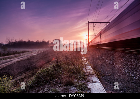 on an early morning at sunrise right next to a passing train with fog banks in the distance Stock Photo