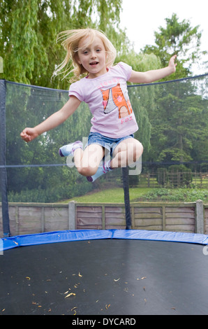 Girl aged 5- 6 on bouncing trampoline in her back garden Stock Photo