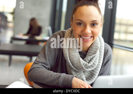 Close up portrait of young african woman sitting in library looking at camera smiling. Female student in university library. Stock Photo
