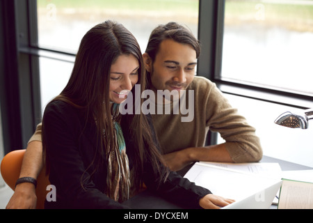 Two young students sitting together at table using laptop. Classmates with books and laptop for finding information. Stock Photo