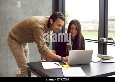 Young woman with her friend at the study desk. Students studying together with laptop. Finding information in library. Stock Photo