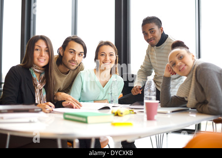 Portrait of a group of positive university students sitting at table in library. Mixed race people studying together in library. Stock Photo