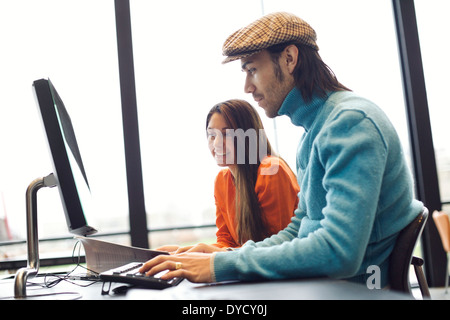Two young people finding information on internet for their academic project. Students sitting at table with book and computer. Stock Photo