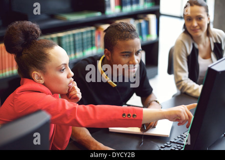 Small group of university students working on computer in a library. Young people finding information for their college. Stock Photo