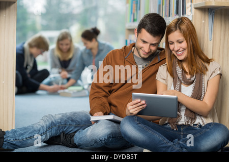 Smiling students using tablet with friends in background at library Stock Photo