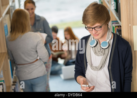 Student with headphones using mobilephone with friends in library Stock Photo