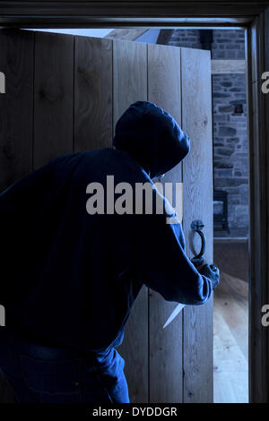 An anonymous hooded male carrying a knife entering a room. Stock Photo