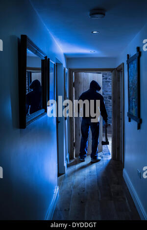 An anonymous hooded male entering a room carrying an axe. Stock Photo