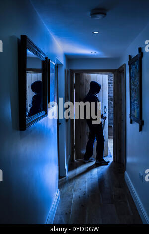 An anonymous hooded male carrying a knife entering a room. Stock Photo