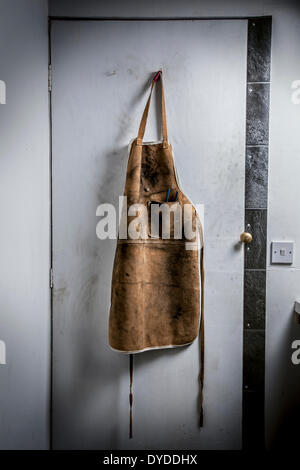 Leather workshop apron hanging on a workshop door. Stock Photo
