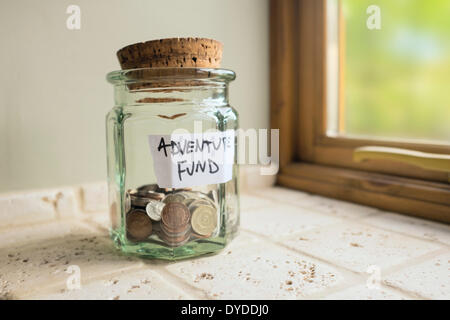 Glass jar labelled Adventure Fund containing loose change. Stock Photo
