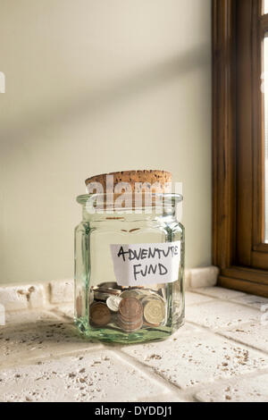 Glass jar labelled Adventure Fund containing loose change. Stock Photo