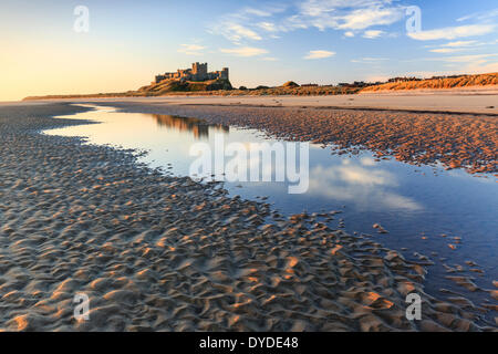 Bamburgh Castle reflected in a tidal pool in early morning sunlight. Stock Photo