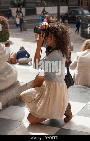 Kneeling young female tourist with camera photographing at St Paul's Cathedral in London. Stock Photo