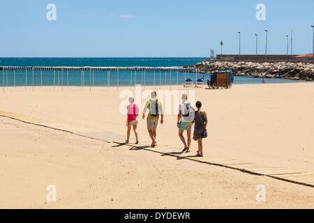 Four people walking down slatted wood access ramp to beach at Cambrils in Spain. Stock Photo