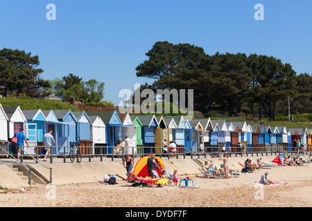 Row of colourful beach huts and holiday makers on the seafront at Mudeford. Stock Photo