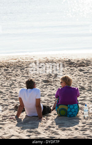 Couple sat alone on a sandy beach enjoying early morning sunlight. Stock Photo