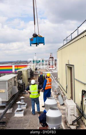 Three workman in high visibility jackets and hard hats guiding crane lift onto roof. Stock Photo