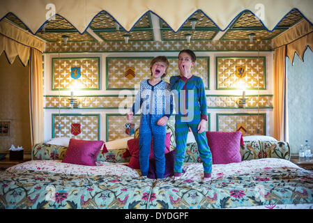 Two boys yawning in onesies on the biggest hotel bed in Europe at Thornbury Castle. Stock Photo