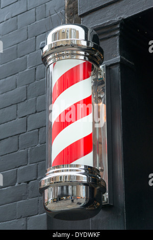 A red and white barber shop pole on a wall outside a shop in the UK