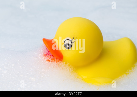 A yellow plastic duck floating in a frothy bubble bath Stock Photo