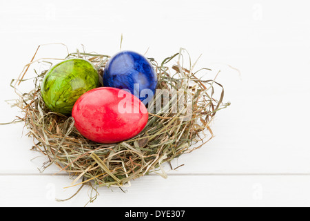 Red, green and blue easter eggs in hay nest on white wooden table Stock Photo