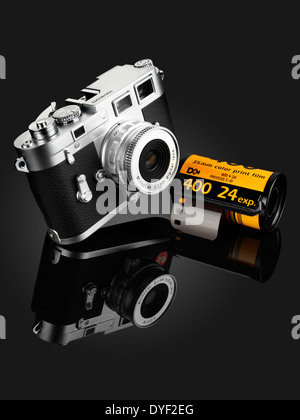 A FUJIFILM SILVER AND BLACK CAMERA WITH A ROLL OF KODAK FILM ON A GRADUATED BLACK BACKGROUND WITH REFLECTION Stock Photo