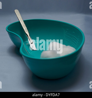 Surgical scalpel in a green plastic kidney bowl on blue surgical drapes. Steel. Knife. Medical instruments. Hazardous. Sharps. Stock Photo