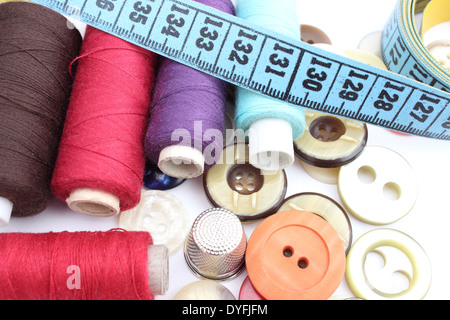 Colorful spools of thread with a tape measure, thimble and buttons isolated on white Stock Photo