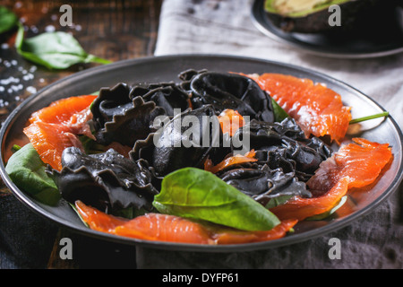 Vintage plate with black homemade ravioli with salted salmon and fresh spinach. Stock Photo