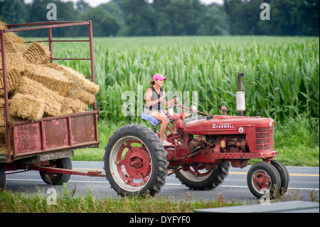 Woman farmer hauling hay wagon with tractor Stock Photo