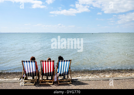 Three people sitting in deck chairs on Southend seafront in Essex. Stock Photo