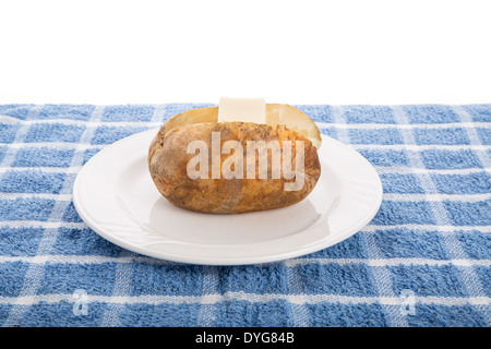 A baked potato with a pat of butter on a white plate and blue towel Stock Photo