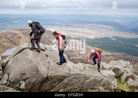 Three hikers scrambling up hill over rocks on Carnedd Moel Siabod Daear Ddu east ridge in mountains of Snowdonia National Park Wales UK Stock Photo