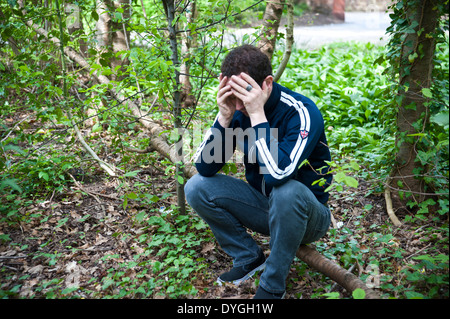 A depressed man sits alone in the woods with his head in his hands Stock Photo