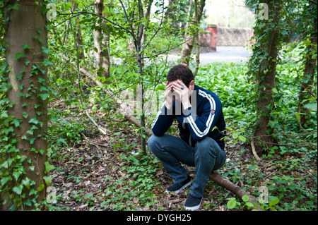 A depressed man sits alone in the woods with his head in his hands Stock Photo