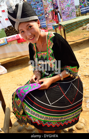 Hmong girl in traditional dress at work embroidering cloth to be made into purses for tourists , open air market, a village near Luang Prabang ,Laos Stock Photo