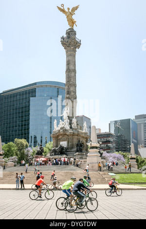 bicyclists enjoy traffic free Paseo de la Reforma  glorieta roundabout below crowd on steps waiting to enter Angel monument Stock Photo