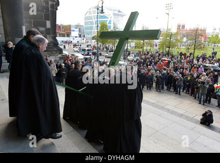 Berlin, Germany. 18th Apr, 2014. Father Bertold Hoecker, cathedral priest Michael Koesling, superintendent general Ulrike Trautwein and cathedral priest Thomas Mueller (R-L), carry a wooden cross during the Good Friday procession outside of the cathedral in Berlin, Germany, 18 April 2014. The procession is a Christian ritual at Easter to reinact the Passion of Christ. Photo: RAINER JENSEN/dpa/Alamy Live News Stock Photo