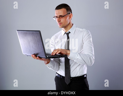 Confident businessman in glasses using laptop over gray background Stock Photo